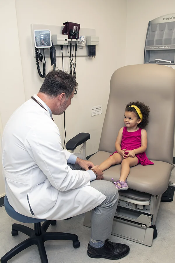 A PCOM physician laughs with a child patient in an exam room